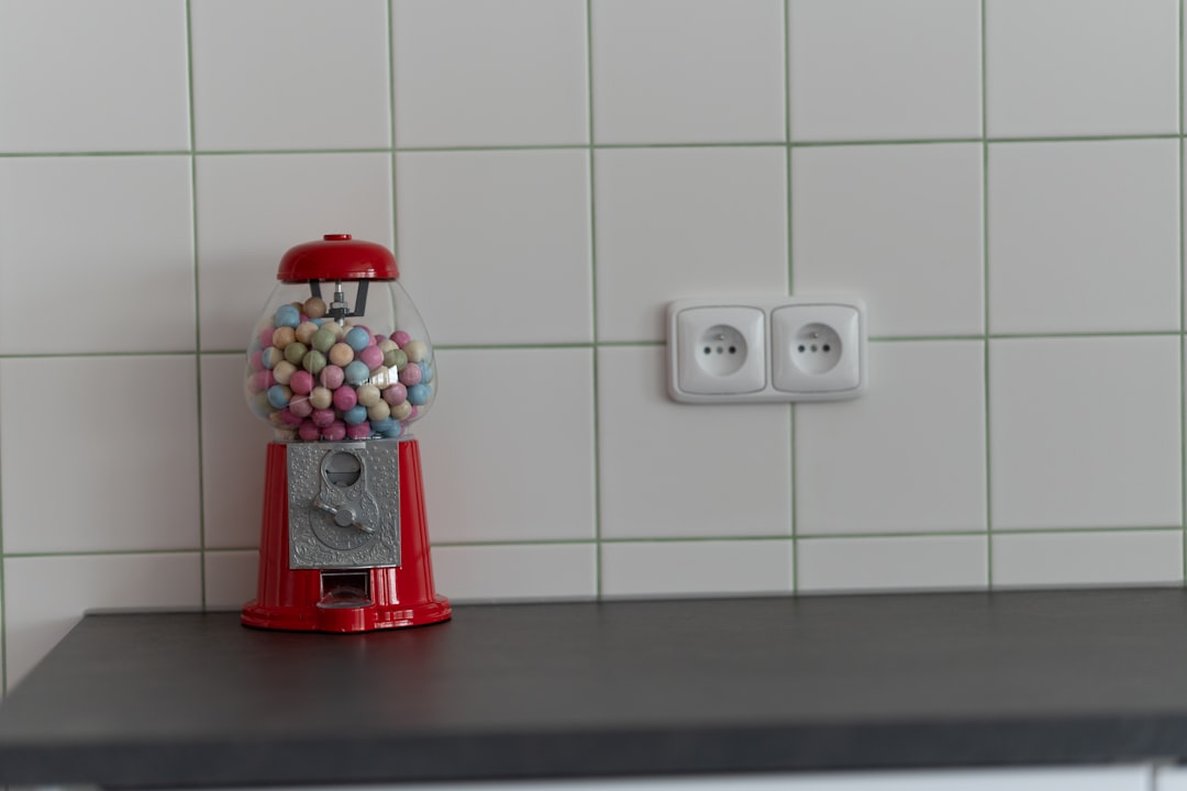 A gumball machine stands next to an electrical outlet.
