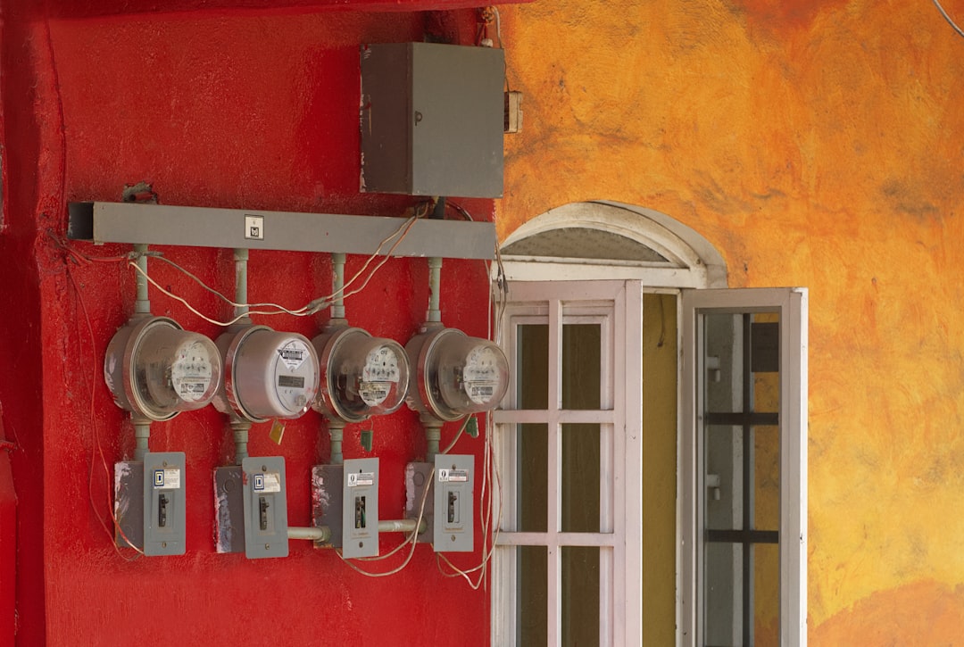 Four electric meters mounted on a red wall.
