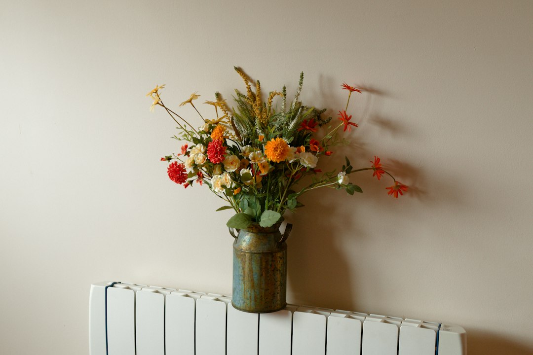 Colorful artificial flowers in a rustic vase on a radiator