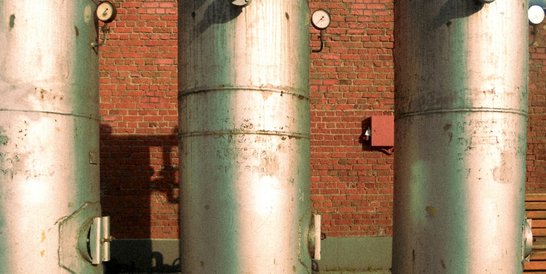 Three tall metal industrial tanks with pressure gauges against a red brick wall