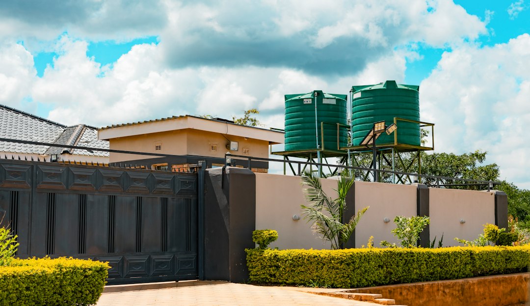 Two green water tanks on metal stands behind a beige wall and gate
