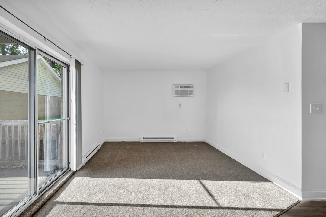 An empty room with brown carpet and a sliding glass door to a patio